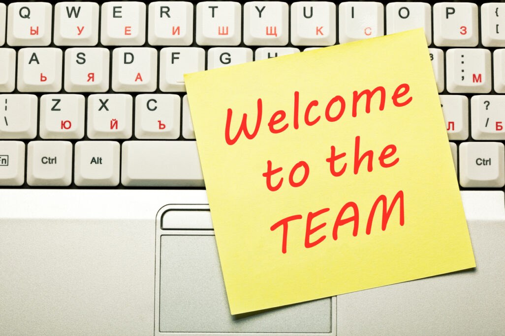 Texto Welcome to the Team (Bem-vindo à equipe) escrito à mão em um bloco de notas amarelo no teclado do laptop