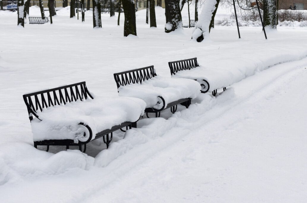 Escena invernal con tres bancos cubiertos de nieve en un parque urbano